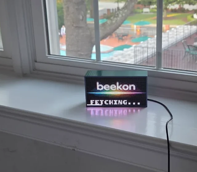 Beekon Light sitting on a white windowsill, plugged in below the window, glowing with its rainbow boot screen